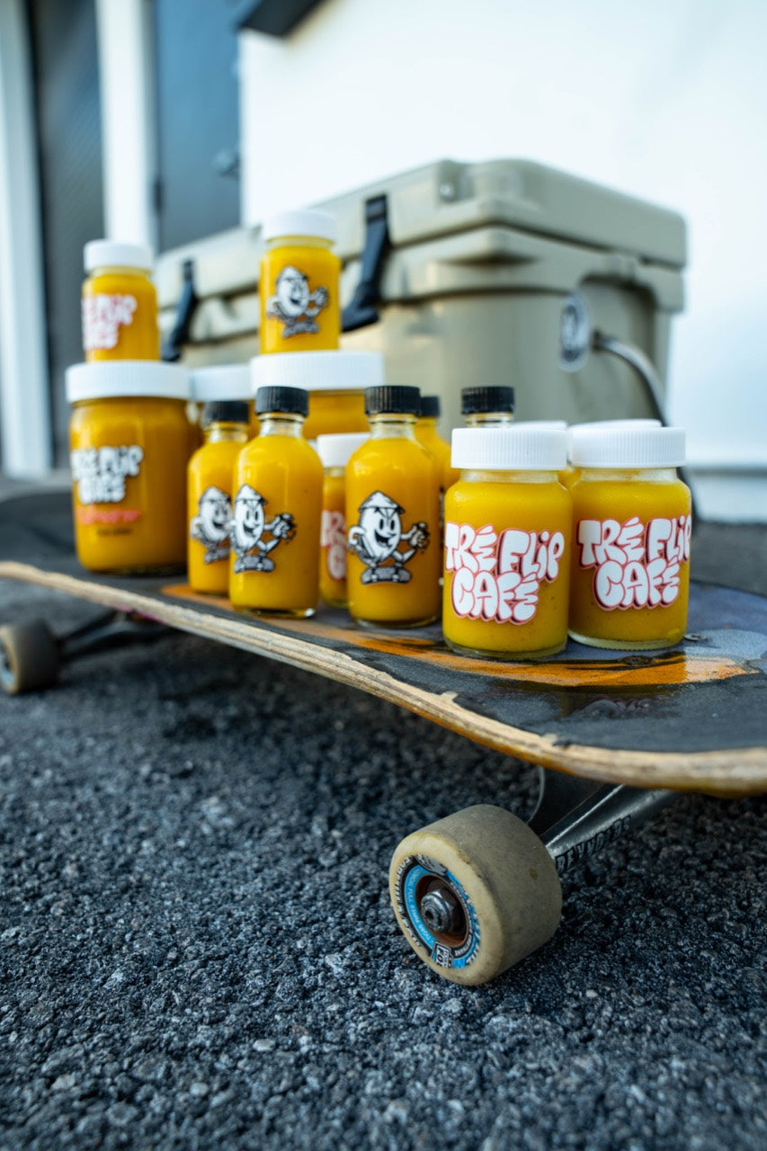 Tre Flip Cafe Classic Ginger OG ginger shots and jars arranged on a skateboard beside a cooler